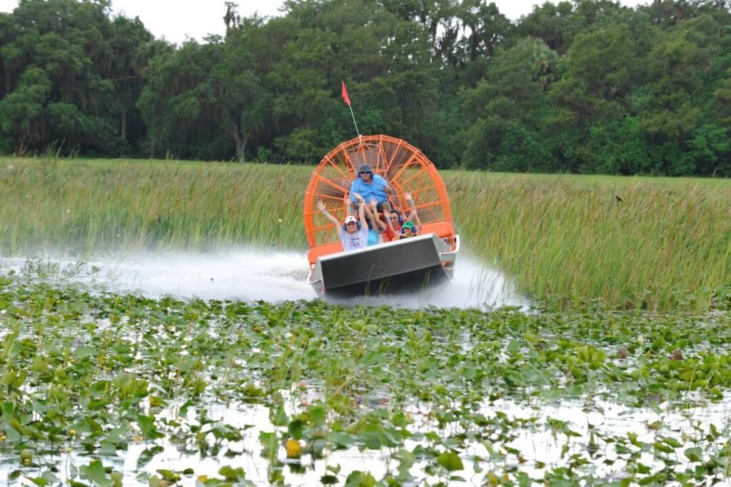 Speeding airboat filled with guests with arms raised up in the air during a Real Florida Adventures tour