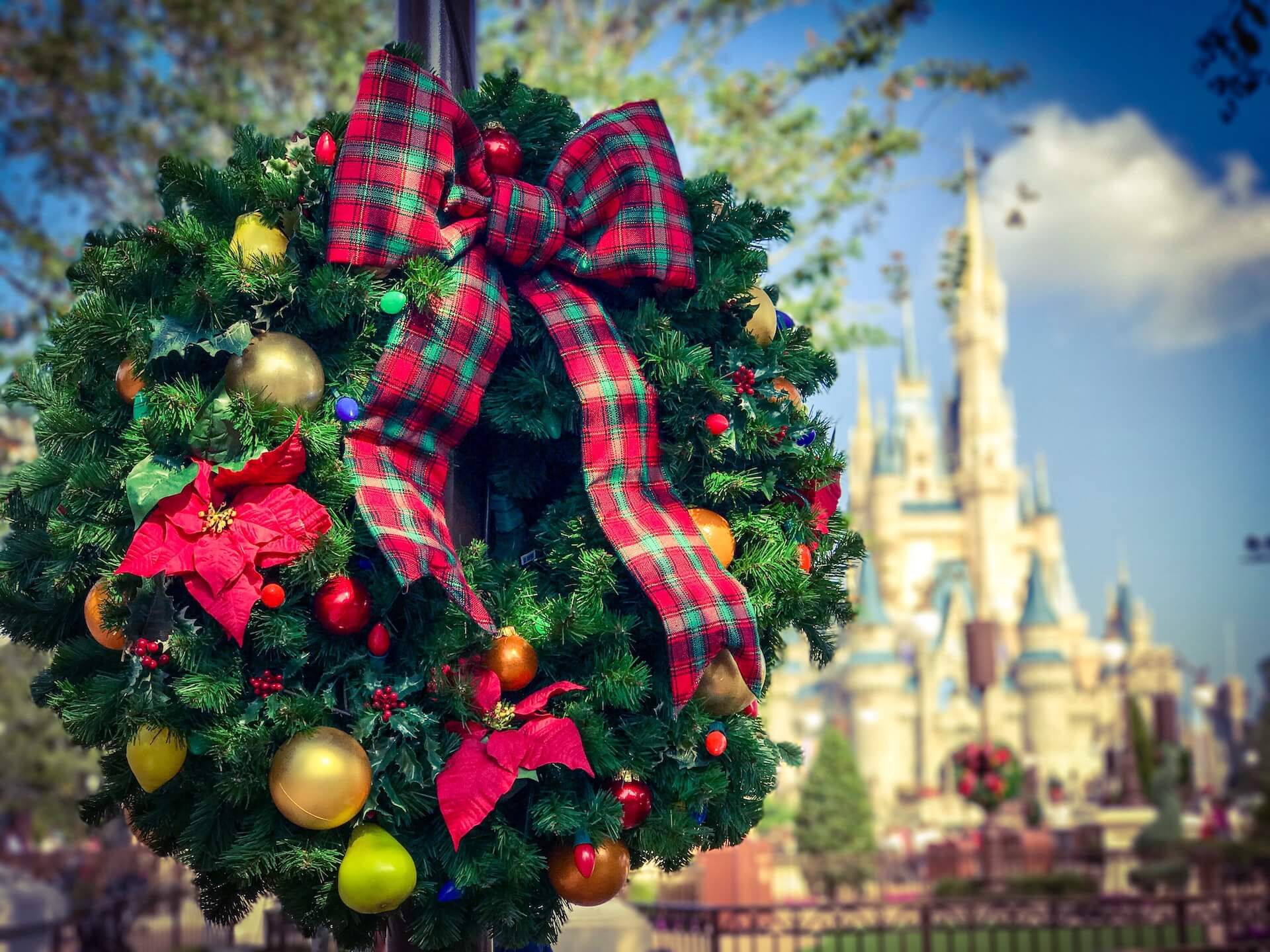 A festive wreath hangs in the foreground, with the Magic Kingdom castle in the background