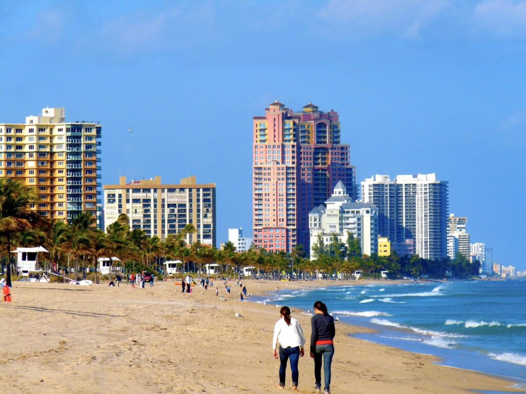 People walking along a beach in Fort Lauderdale with high rises in the distance