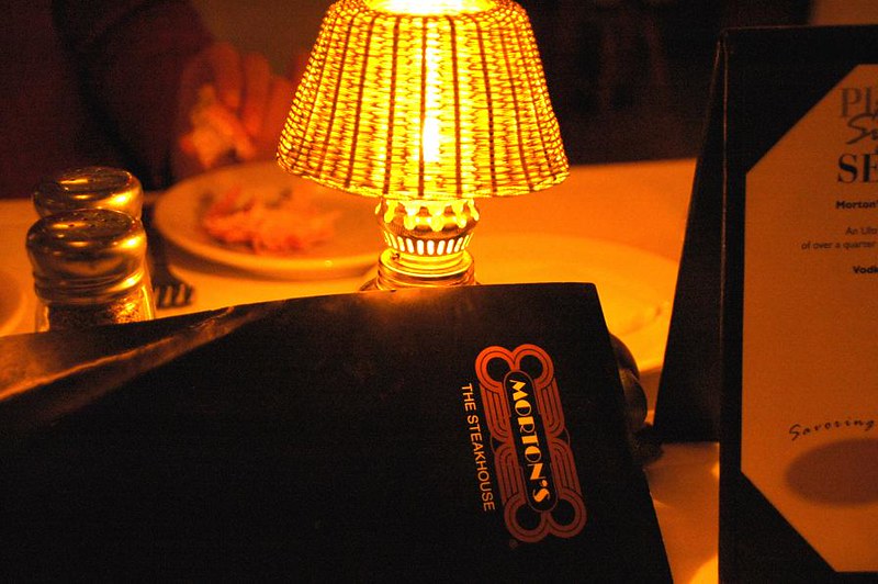 Morton's Steakhouse menu illuminated by a table lamp.